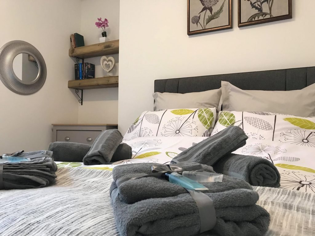 Double bed with green and white bedding, folded grey towels and Scottish thistle artwork at King Street Holiday Apartment